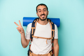 Young caucasian hiker man isolated on blue background joyful and carefree showing a peace symbol with fingers.
