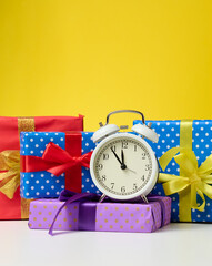 Wall Mural - round alarm clock and a stack of gift boxes tied with a ribbon on a yellow background. Christmas and New Year