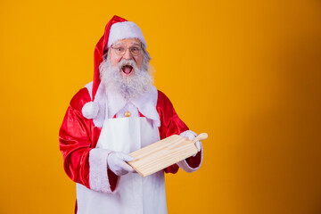 Santa Claus dressed in apron holding empty meat board on yellow background.