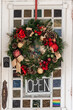 Vintage, Old, rustic weathered, white wooden store entry doorway with Traditional christmas wreath and garland with red ornaments and gold baubles