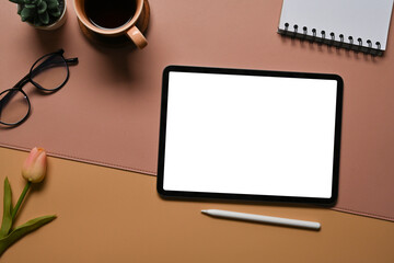 Poster - Top view image of a white blank screen digital tablet with a stylus pen putting on a working desk surrounded by a notebook, coffee cup, potted plant, eyeglasses and flower.