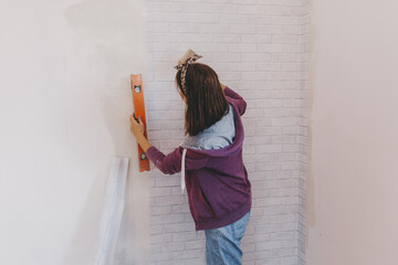 Wall Mural - Young woman glues wallpaper at home. girl glues wallpaper in the form of a brick. repair.