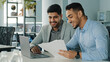 © Yuliia - Cheerful positive friendly businessmen partners colleagues holding document contract looking at laptop screen discuss ideas having fun during break in office. Good business relationships, concept