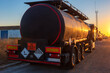 Black tanker truck for the transport of dangerous goods, in front of a street at sunset.