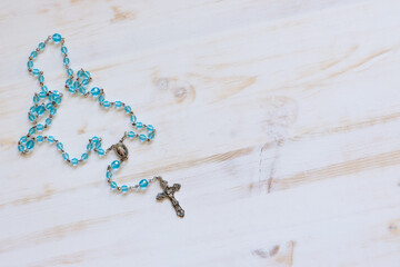 Rosary with crystal blue beads on a white wood background with copy space