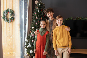 Sticker - Portrait of smiling middle-aged woman with short curly hair embracing two children against Christmas tree