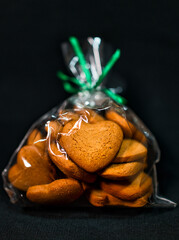 Sticker - Vertical shot of heart-shaped cookies in a clear plastic bag with green ties on a black background