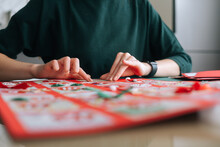 Close-up Of Unrecognizable Young Woman Gluing Envelopes On Board With Gifts For Children Making Christmas Advent Calendar At Home, Selective Focus, Blurred Background. Preparing For Xmas, New Year.