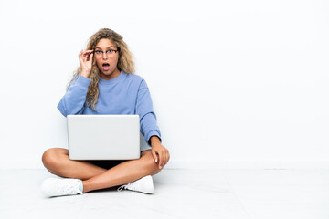 Wall Mural - Girl with curly hair with a laptop sitting on the floor with glasses and surprised