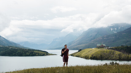 Wall Mural - man posing on a mountaintop with hotel and lake in the background