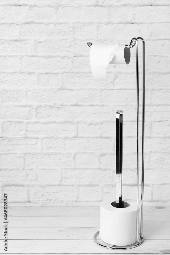 Holder with cardboard tube and toilet paper rolls on wooden floor near white brick wall