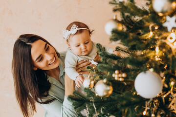 mother with baby daughter dacorating christmas tree