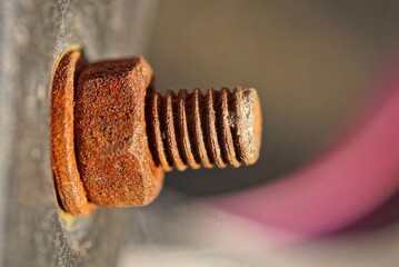 one big old brown red rusty bolt with a twisted nut on a gray metal wall