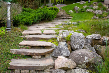 Wall Mural - stone staircase with steps made of wild natural stone on slope of hill park landscape with bushes and trees, ground garden lantern among green plants in summer eco environment, nobody.