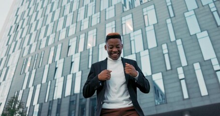 Wall Mural - Joyful, positive man dressed in suit stands outside in front of glass building of company, corporation, office worker received good news happy dancing waving hands satisfaction promotion, salary