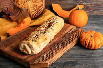 Board with tasty pumpkin strudel on wooden background, closeup