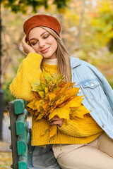 Wall Mural - Dreamy woman with autumn bouquet sitting on bench in park