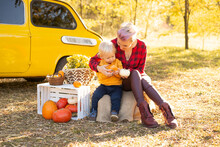 Happy Mother And Baby Boy With Flowers And Pumpkins In Autumn Park Background And Yellow Car