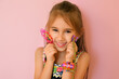 © Maryna - Cute girl with braided bracelets on her wrist holds a loom with an unfinished bracelet and a slingshot for weaving from rubber bands, isolated on a pink studio background. funny laughing baby