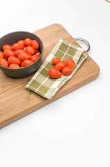 Poster - datterini tomatoes in a dark bowl with chopping board and table napkin on a white background