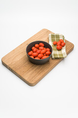 Poster - datterini tomatoes in a dark bowl with chopping board and table napkin on a white background