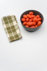 Poster - datterini tomatoes in a dark stoneware bowl and table napkin on a white background