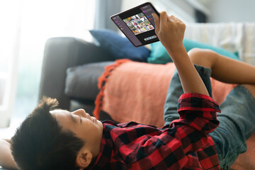 Wall Mural - Asian boy using tablet for video call, with smiling diverse elementary school pupils on screen