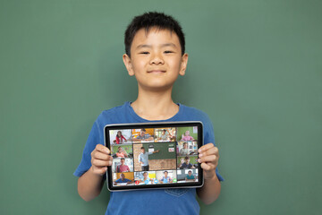 Poster - Smiling asian boy holding tablet for video call, with diverse elementary school pupils on screen