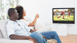 Rear view of african american couple sitting at home together watching hockey match on tv
