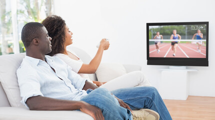 Canvas Print - Rear view of african american couple sitting at home together watching athletics event on tv