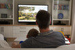 Rear view of father and son sitting at home together watching sport event on tv