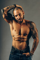 Wall Mural - A brutal Latin American or Cuban with tattoos on his body poses on a gray background. A middle-aged man with a muscular pumped body. Studio portrait