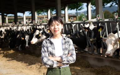 Portrait of chinese female farmer who is standing at her workplace near cows at the farm outdoors. High quality photo