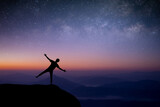 Fototapeta Kosmos - Silhouette of young traveler and backpacker standing and open arm looking the star and Milky Way alone on top of the mountain. He enjoyed traveling and was successful when he reached the summit.