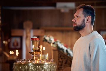 Wall Mural - a bearded man in a headscarf prays in an Orthodox church and puts candles in front of icons