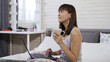 © PRPicturesProduction - smiling pretty asian chinese lady enjoying the fragrance of the coffee alone in the bedroom while using laptop in comfortable white bed