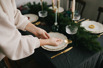 Young woman serving Christmas table with beautiful festive tableware. Preparations for holiday dinner.