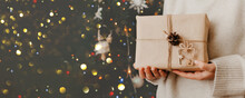 Girl Holding Small Gift In Her Hands. Decorated Christmas Tree On Background. Bright Christmas Card With Space For Text