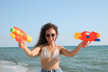 Wall Mural - African American woman with water guns having fun on beach