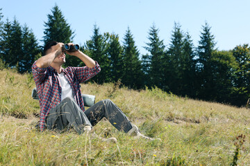 Poster - Tourist with hiking equipment looking through binoculars outdoors