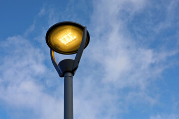 Glowing led lamp on background of blue sky with white clouds. Electric lighting, energy-saving street lantern