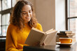 © Drobot Dean - Young white woman reading book while drinking coffee in cafe