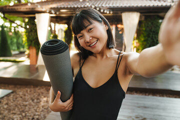 Wall Mural - Asian woman taking selfie photo while standing with yoga mat