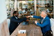 © Drobot Dean - Multiracial men handshaking while working with laptops in cafe