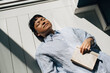 © Maskot - Young woman lying on floor with book in sunlight at home