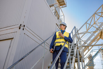 Smiling man factory worker holding takeaway drink and folder while standing on staircase outside industrial building