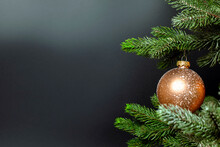 One Single Christmas Bauble Hanging On Fresh Green Branch Of Christmas Tree Near Dark Black Background With Copy Space, Merry Christmas, Holiday Concept
