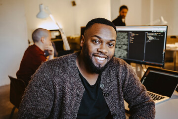 Portrait of young male programmer by colleague working at desk in startup company