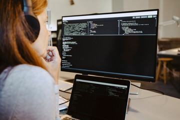 Female hacker looking at codes over computer screen in creative office