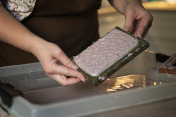 A woman holding a frame for making paper sheets from recycled paper. Selective focus. Household hobby, paper recycling. The concept of zero waste, recycling, ecology